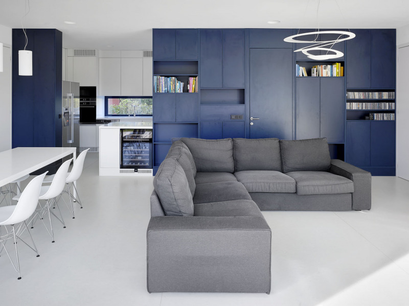 Architekti navrhli také interiér domu, který byl vybaven vestavěným nábytkem na míru, převážně z lakovaných MDF desek. Střízlivé tvary a kombinace šedé, bílé a modré působí neutrálním dojmem, záměrem bylo obrátit pozornost především do zahrady. „Hledali jsme s majiteli barvy, které mají rádi, které je uklidňují a jsou nadčasové a elegantní. V obytném prostoru zvítězila tmavě modrá, kterou jsme použili i na okna. Do koupelny pak to byla sytě žlutá – teplý odstín, který koupelnu ‚zahřeje‘. Barevná kombinace je inspirovaná 30. léty 20. století, stejně jako racionální uspořádávání celého domu,“ říká architekt Tesař. Kuchyň je od obývacího pokoje částečně oddělena nábytkovou stěnou navrženou na míru. Kromě otevřených knihoven obsahuje cenné úložné prostory a její nenápadnou součástí jsou i dveře do chodby