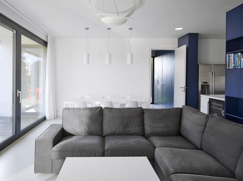 Architekti navrhli také interiér domu, který byl vybaven vestavěným nábytkem na míru, převážně z lakovaných MDF desek. Střízlivé tvary a kombinace šedé, bílé a modré působí neutrálním dojmem, záměrem bylo obrátit pozornost především do zahrady. „Hledali jsme s majiteli barvy, které mají rádi, které je uklidňují a jsou nadčasové a elegantní. V obytném prostoru zvítězila tmavě modrá, kterou jsme použili i na okna. Do koupelny pak to byla sytě žlutá – teplý odstín, který koupelnu ‚zahřeje‘. Barevná kombinace je inspirovaná 30. léty 20. století, stejně jako racionální uspořádávání celého domu,“ říká architekt Tesař. Kuchyň je od obývacího pokoje částečně oddělena nábytkovou stěnou navrženou na míru. Kromě otevřených knihoven obsahuje cenné úložné prostory a její nenápadnou součástí jsou i dveře do chodby