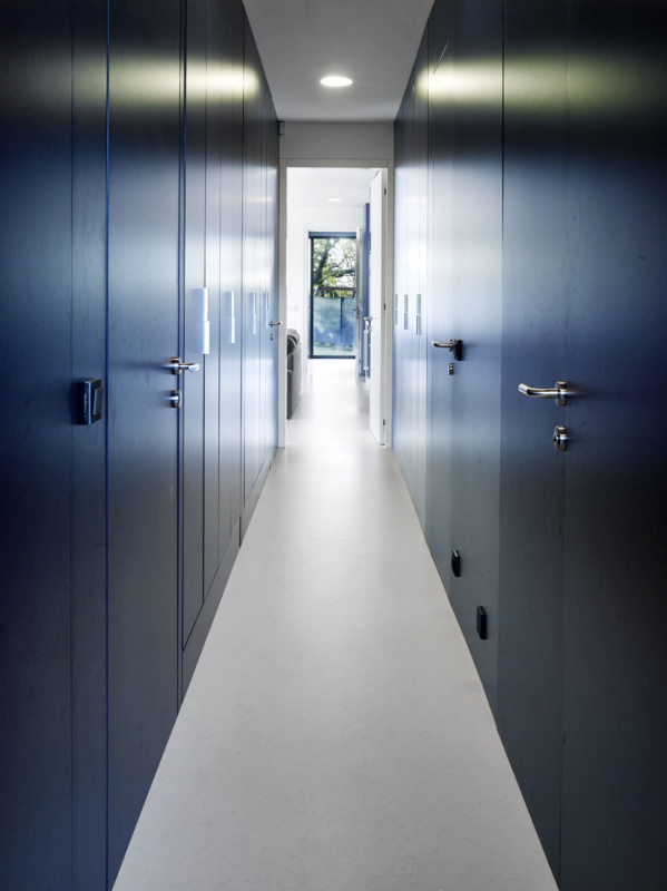 Architekti navrhli také interiér domu, který byl vybaven vestavěným nábytkem na míru, převážně z lakovaných MDF desek. Střízlivé tvary a kombinace šedé, bílé a modré působí neutrálním dojmem
