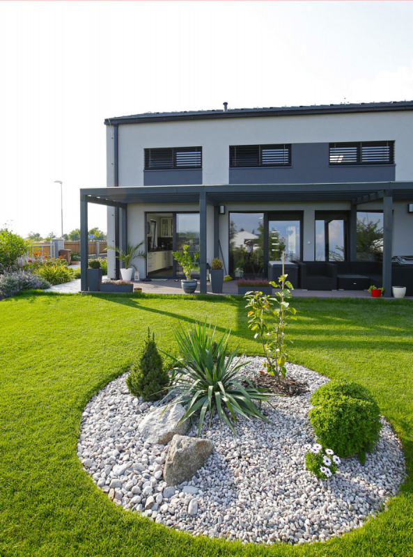 Společný obývací prostor lemuje dřevěná pergola přistavěná po celé jeho délce. Šedý nátěr dřevěných profilů je v jednotě s fasádou i betonovou střešní krytinou a budí dojem kovové konstrukce