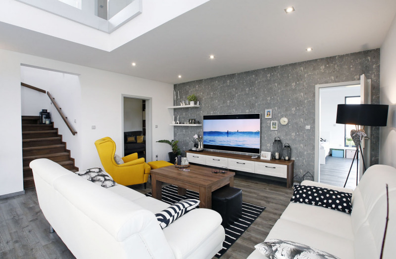 Společný obývací prostor s průhledem nahoru na galerii v patře. Do neutrální barevnosti vnáší život žluté křeslo a kontrastní černobílé doplňky