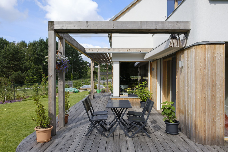 Interiér bezprostředně navazuje na dřevěnou terasu s masivní pergolou a permakulturní zahradu s přírodním jezírkem