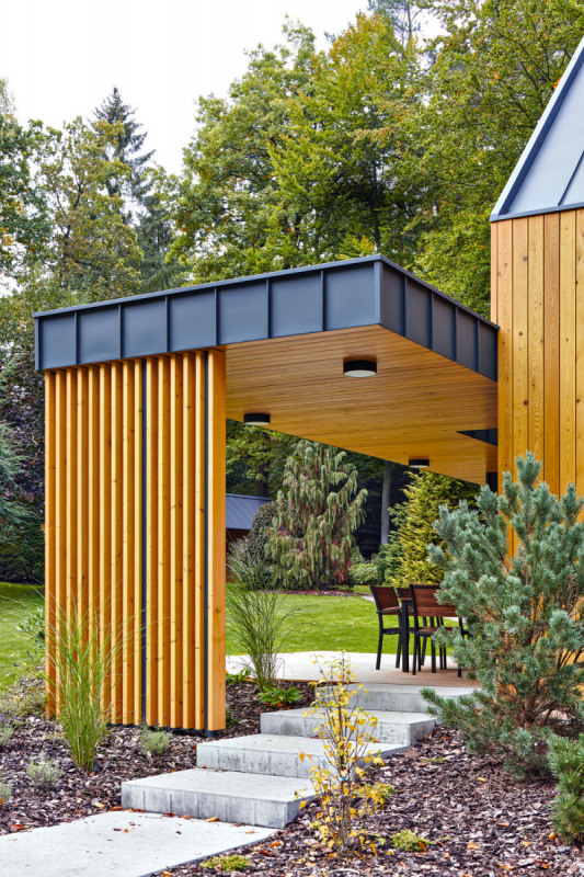 Na střechu přístavby plynule navazuje zastřešení terasy, pod kterým se nachází kryté sezení s výhledem do zahrady. Zajímavým prvkem je svislé laťování