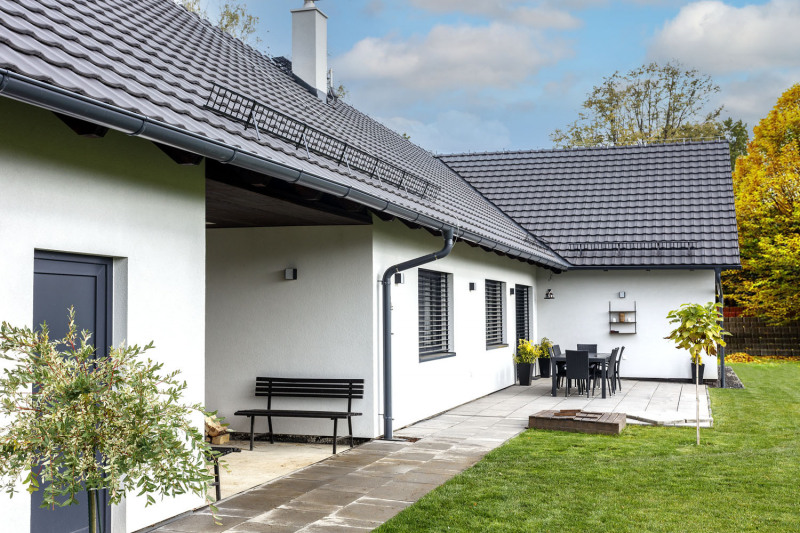 Předokenním venkovním žaluziím pomáhá při stínění přesah střechy. Prostor za domem je částečně vydlážděn, zbytek je zatravněn. Vnitřní roh písmena L je využit pro venkovní posezení