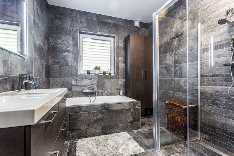 Koupelna využívá mramorově šedých obkladů stěn, podlahy i vany. Naproti dvojitému umyvadlu se nachází minimalistický sprchový kout
