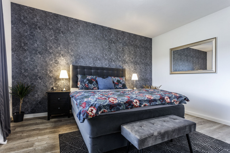 Interiér ložnice skvěle pracuje s barevnými kombinacemi. Barva stěny za pelestí koresponduje s barvou postele, taburetu a kobercem