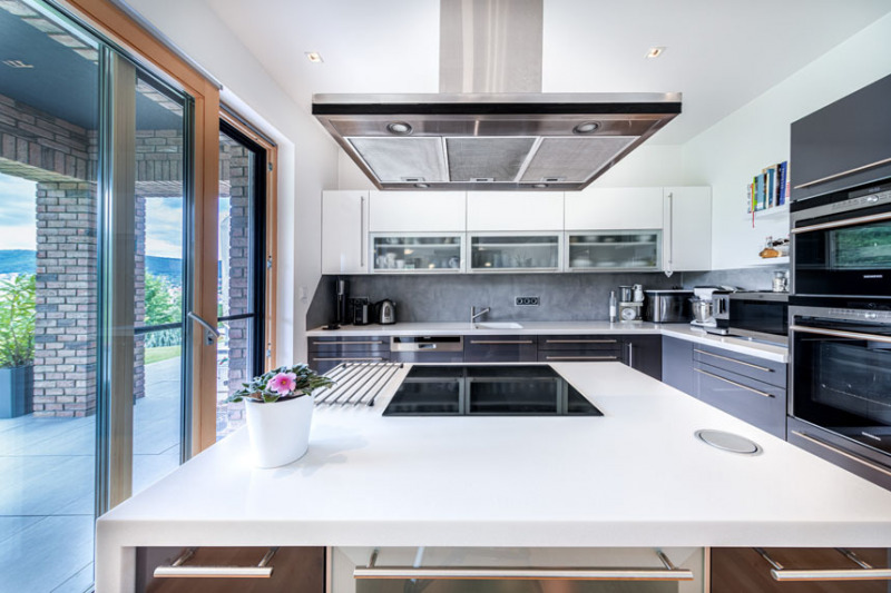 Z kuchyně se dá vyjít přímo na krytou terasu, kde rodina v létě také stoluje. Kuchyňskou linku vyrobilo místní kuchyňské studio na míru z laminovaných MDF desek s příjemným jemně matným povrchem. Je vybavena spotřebiči Siemens a pracovní deskou z odolného kompozitního materiálu Corian