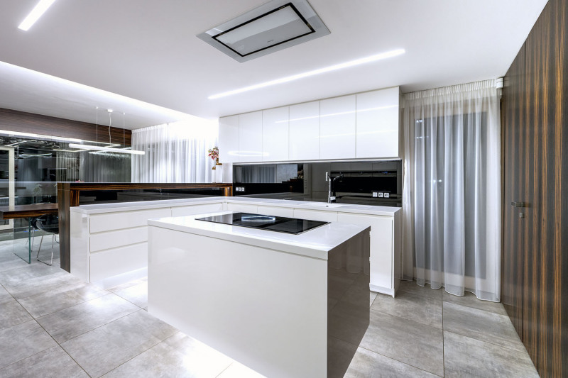 Čisté tvary kuchyně podtrhují kombinaci černého skla, bílého lesklého laku a makassarové dýhy. Veškeré technologie jsou integrovány včetně LED osvětlení a stropní digestoře