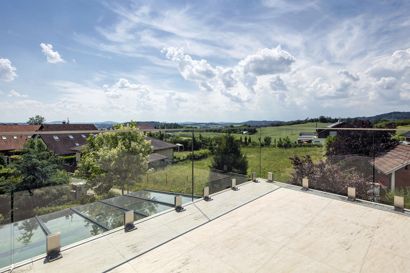 Rozsáhlá terasa v patře je ohraničena minimalistickým zábradlím z čirého kaleného skla, které nebrání výhledu na nádherné okolní panorama