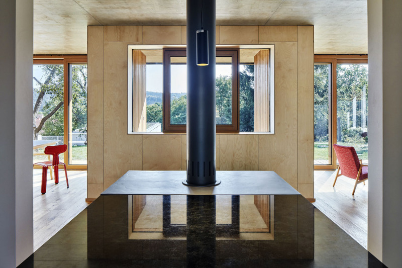 Pohled z kuchyně na zapuštěnou terasu. Jídlo se podává ven oknem vsazeným do pevně zasklené plochy. Pohledový beton na stropě krásně ladí se strukturou světlého dřeva