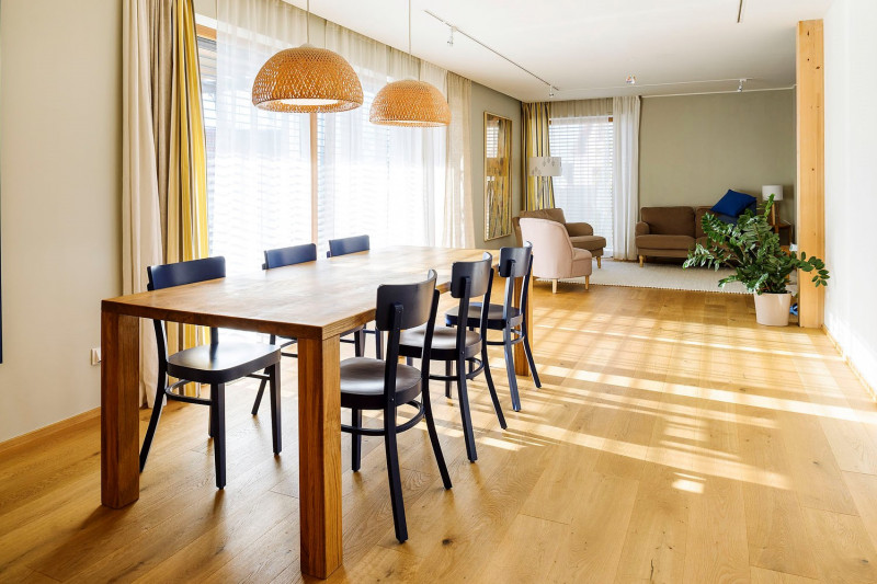 Praktická dispozice domu odpovídá současným trendům – dostatek světla, jednoduché linie doplněné přírodními materiály. V popředí je vidět jídelní stůl pro společné stolování rodiny