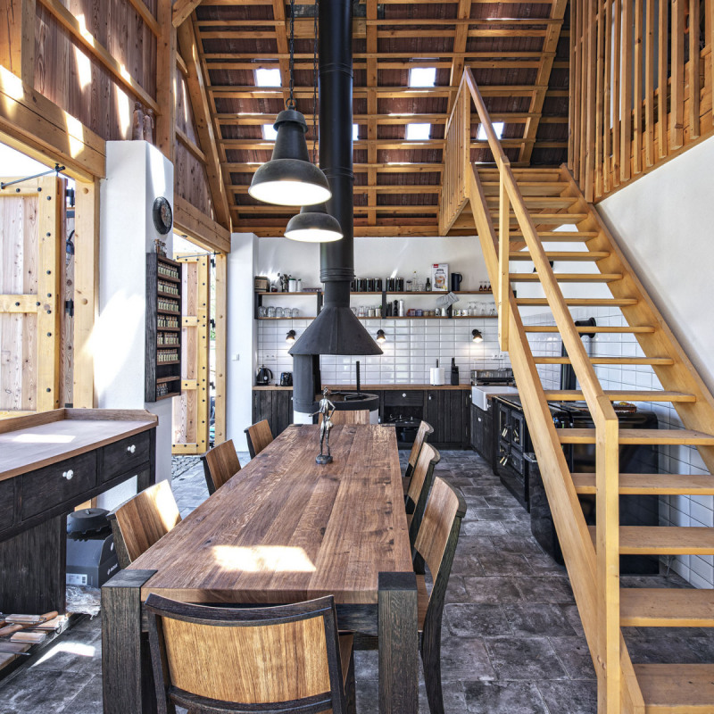 Černá kuchyň ve stodole podle návrhu architektů. Dominantou je otevřený pohled do krovu, otevřené ohniště a kuchyňská linka s masivním dřevěným stolem pro 8 osob