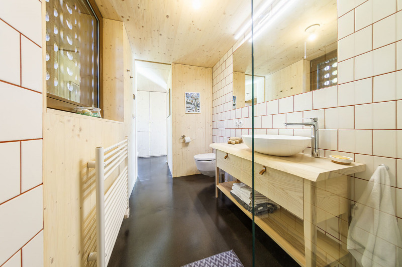 Také koupelna v přízemí je vybavena nábytkem a obklady ze smrkové biodesky. Prostor prosvětlují i bílé obklady a velké zrcadlo
