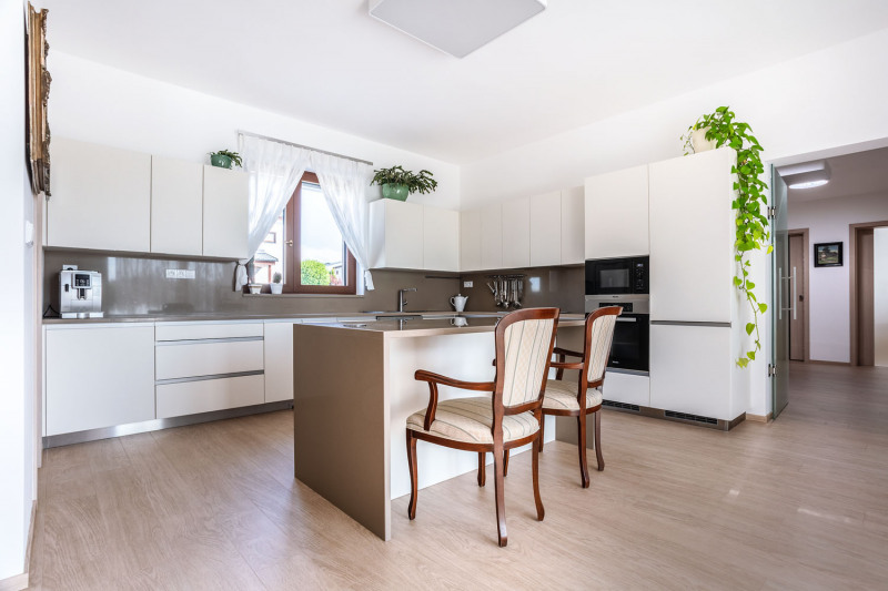 Komfortní rohovou kuchyň doplňuje pracovní ostrůvek. Linka byla vyrobena na zakázku z bíle lakovaných MDF desek a doplněna kvalitní pracovní deskou z umělého kamene