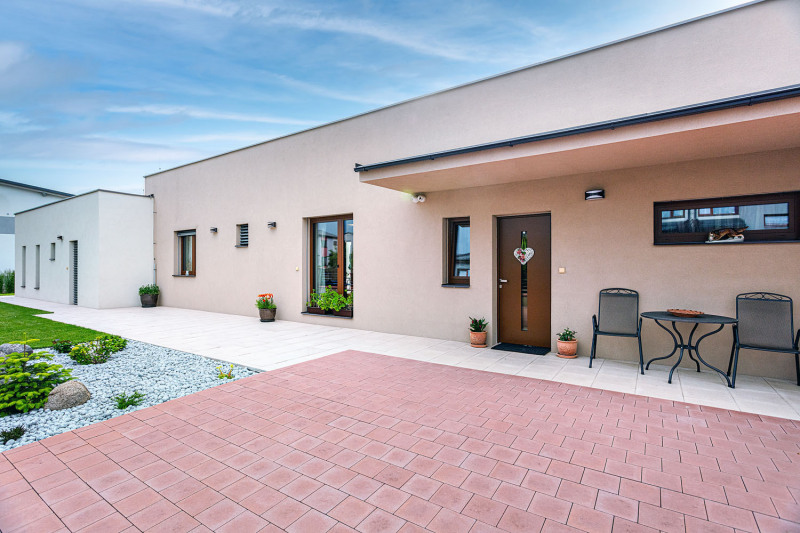 K domu se přichází po zpevněné ploše se zámkovou dlažbou. Vstup je upraven jako útulné a vstřícné zápraží, vchodové dveře chrání stříška směřující ke garáži