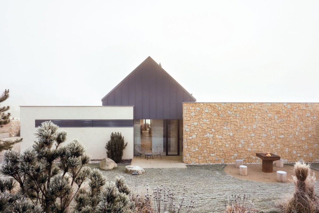 Moderní rodinný dům se sedlovou střechou, kamennou zdí a venkovním posezením s ohništěm