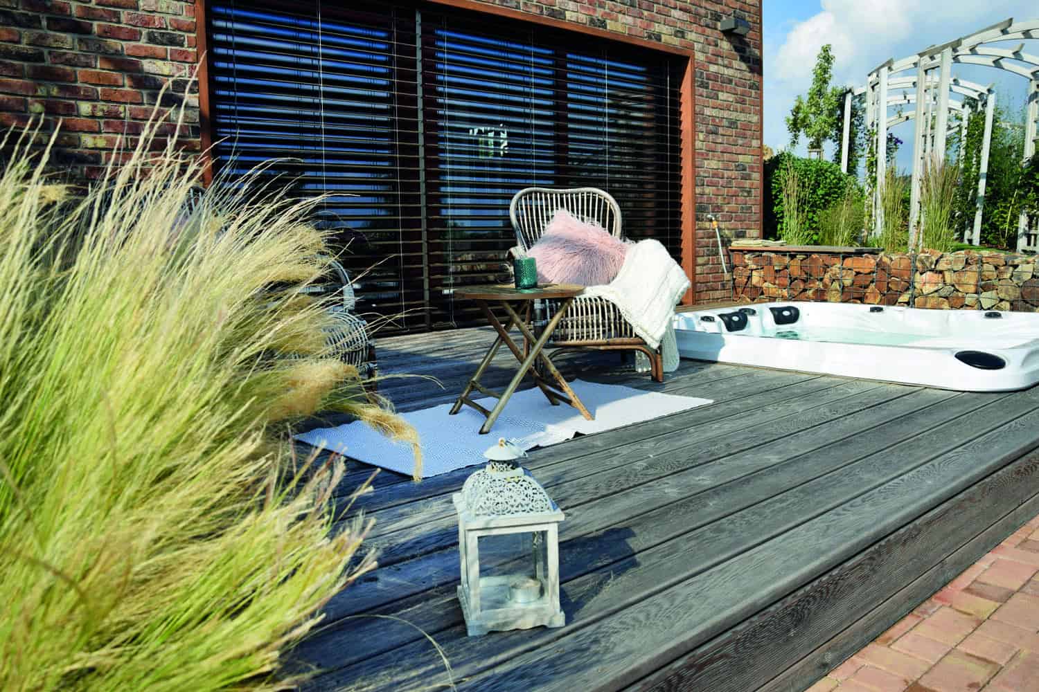 Dřevěná terasa s vířivkou, ratanovým posezením a dekoracemi u moderního domu